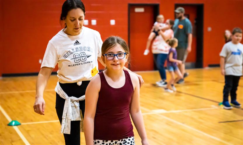 A girl wearing a red tank top walks in a school gym